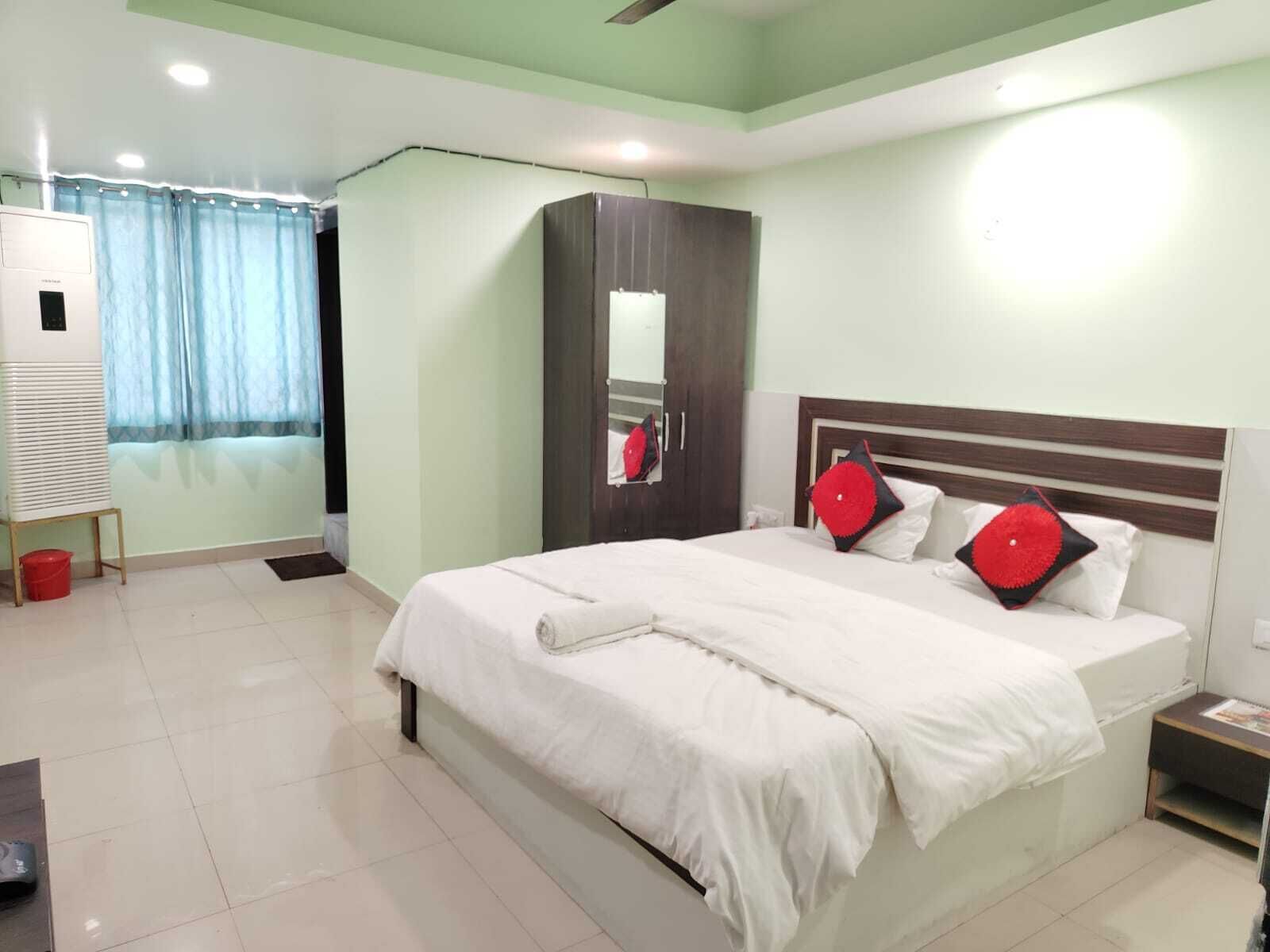 Quarto de hotel com uma cama grande, um guarda-roupa, um espelho e uma janela com cortinas.