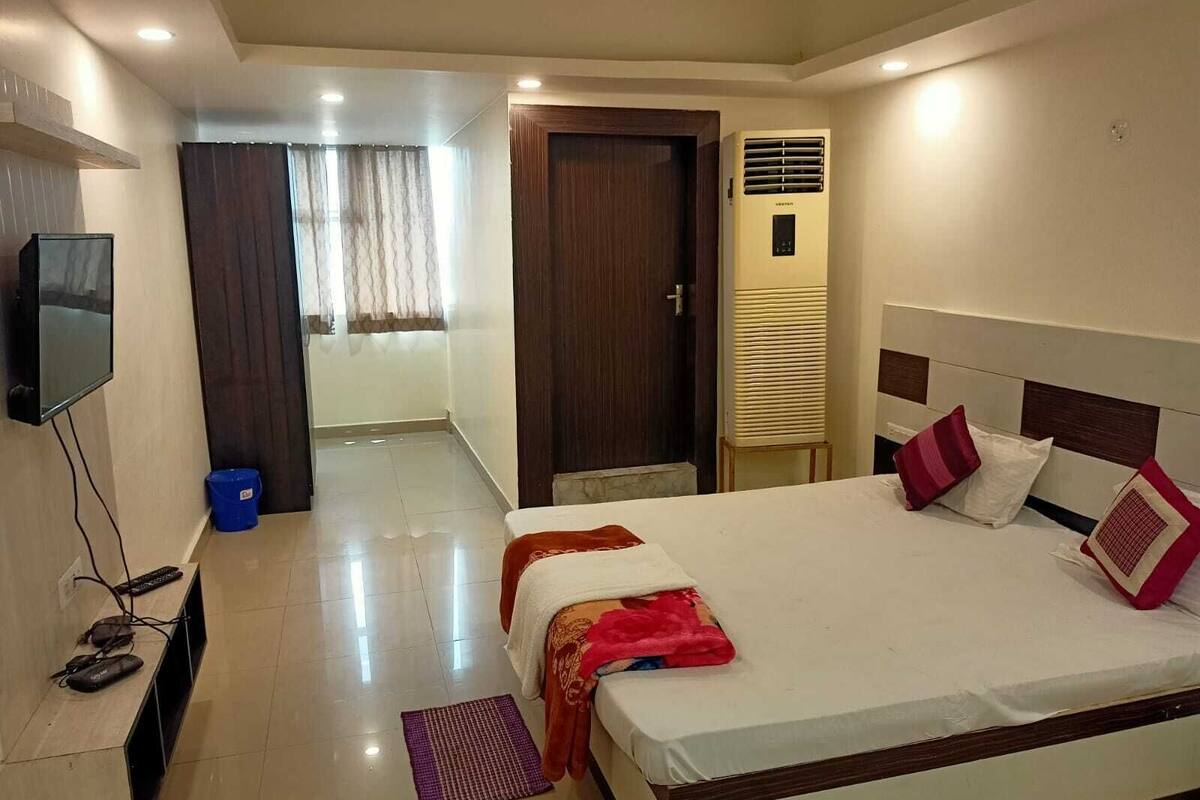 A hotel room with a bed, a TV mounted on the wall, a heater, and a door leading to another room.