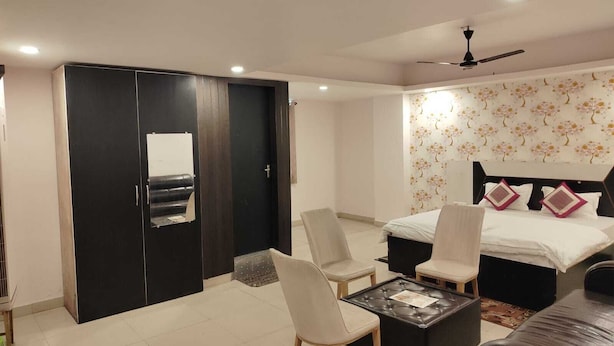 A modern bedroom with a bed, two chairs, a coffee table, a wardrobe, and a ceiling fan. - Raj Mahal Rooms & Banquet Hall (Patna)