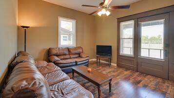 A living room with a leather sectional sofa, a wooden coffee table, a ceiling fan, and a television.