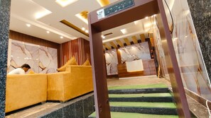 Zona de recepción con pared de mármol, mostrador de recepción y sofá amarillo.