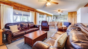 A spacious living room with leather sofas, a wooden coffee table, and a dining area with a wooden table and chairs. - Lake Winnott Home w/ Boat Ramp & Dock (Hawthorne)