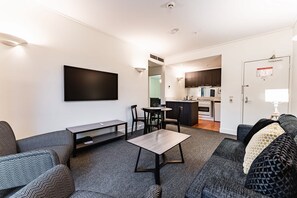 A modern living room with a flat-screen TV, a dining table, and a kitchen area with cabinets and appliances. - Chic 1-Bed in East Melbourne with Gym & Pool (East Melbourne)