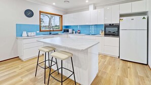 Eine moderne Küche mit weißen Schränken, einer großen Kochinsel mit Barhocker, einer Mikrowelle, einem Backofen und einem Kühlschrank.