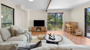 Ein Wohnzimmer mit einer Couch, einem Couchtisch, einem Fernseher und einem Balkon mit Blick auf Grünflächen.