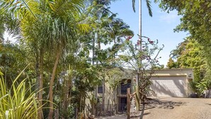 Ein Wohnhaus mit Auffahrt zu einer Garage, umgeben von üppiger Vegetation und Palmen.