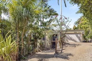 A residential property with a driveway leading to a garage, surrounded by lush greenery and palm trees. - Beachside 4-Bed Retreat with Study Nook & Views (Coolum Beach)