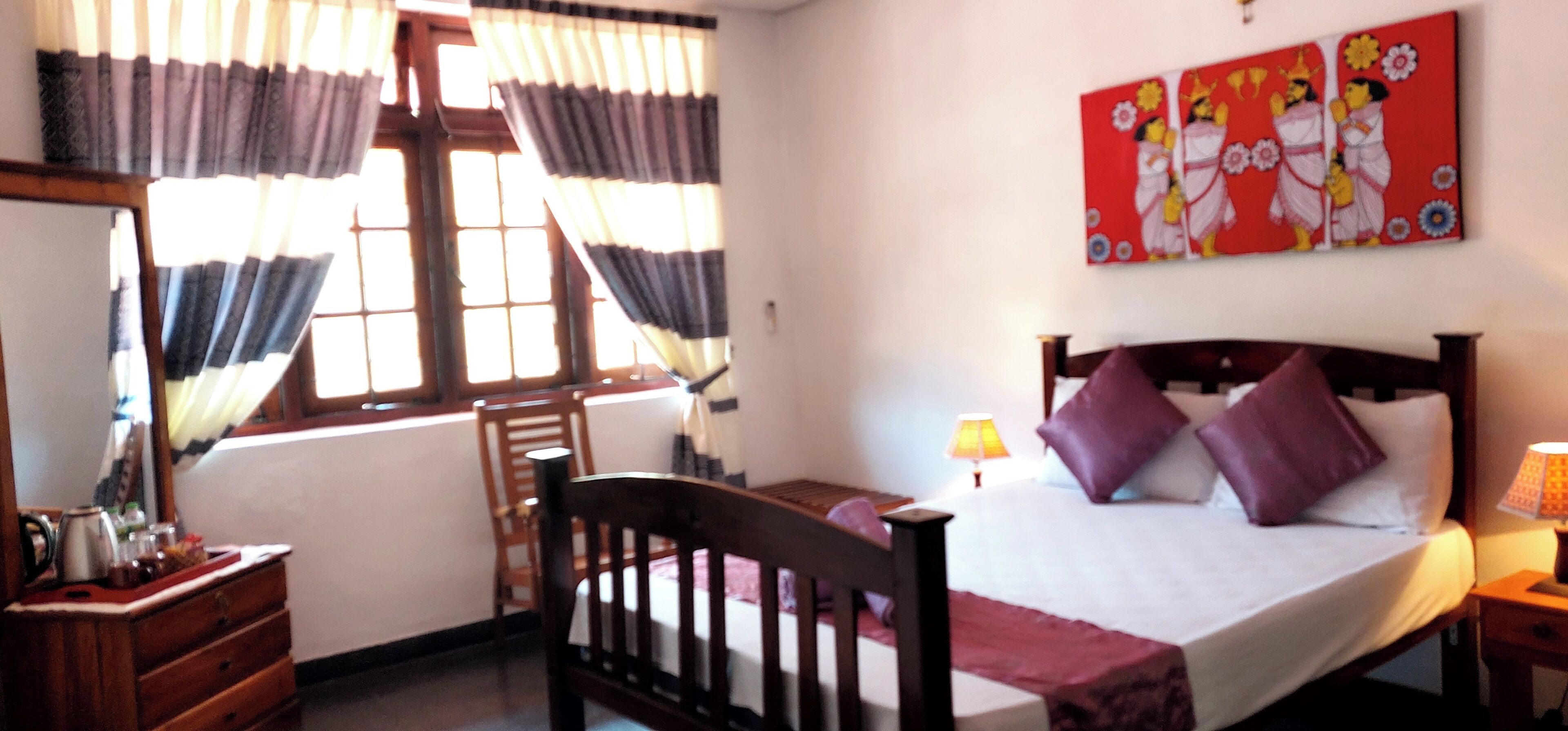 A bedroom with a bed, a wooden chair, a dresser, a window with curtains, and a painting on the wall.