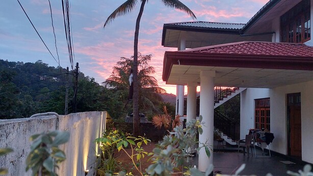 Un edificio con un porche cubierto, una escalera y vistas a un atardecer.