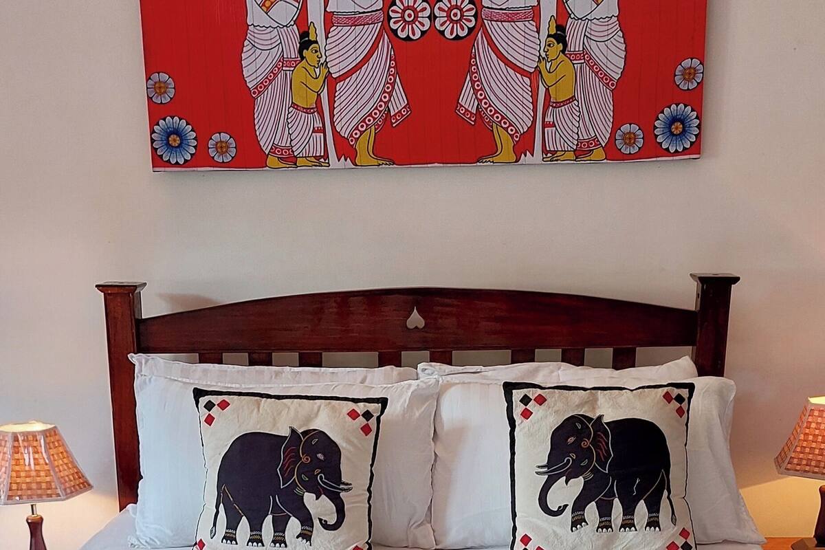 A bed with two pillows featuring elephant designs, a wooden headboard, and a red wall with a cultural painting above.