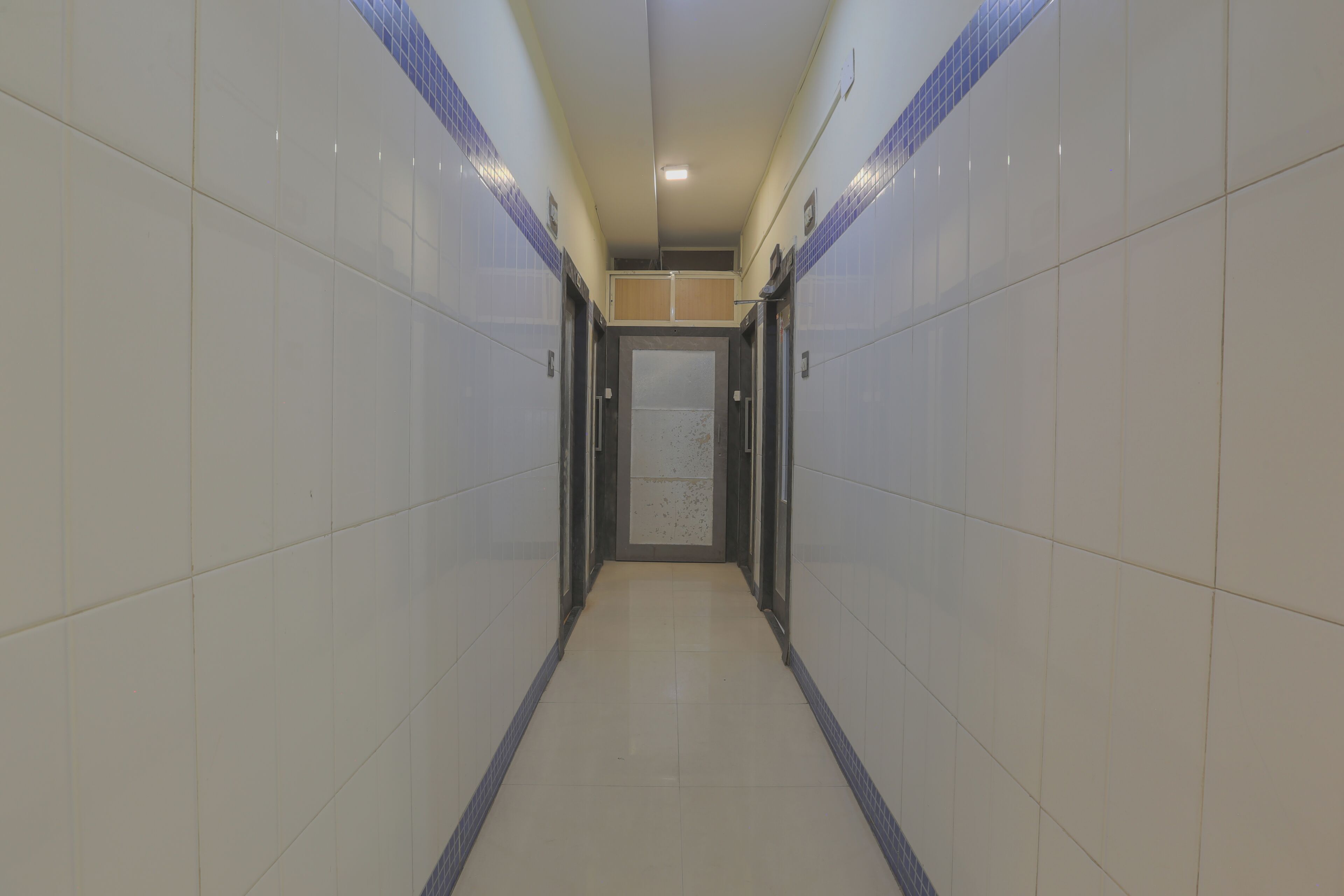 A corridor with tiled walls and a tiled floor, leading to a door at the end.