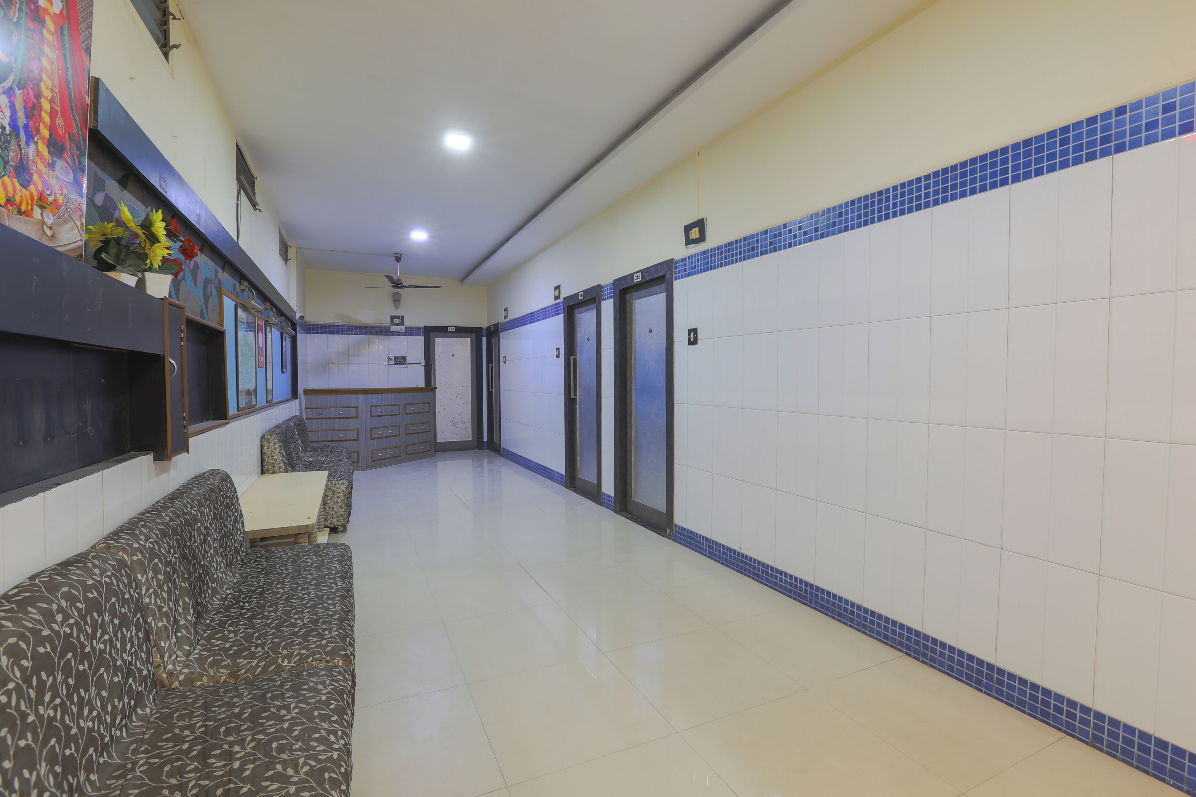 A hotel lobby with a sofa, a small table, a ceiling fan, and a tiled wall with a blue border.