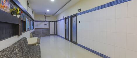 A hotel lobby with a sofa, a small table, a ceiling fan, and a tiled wall with a blue border.