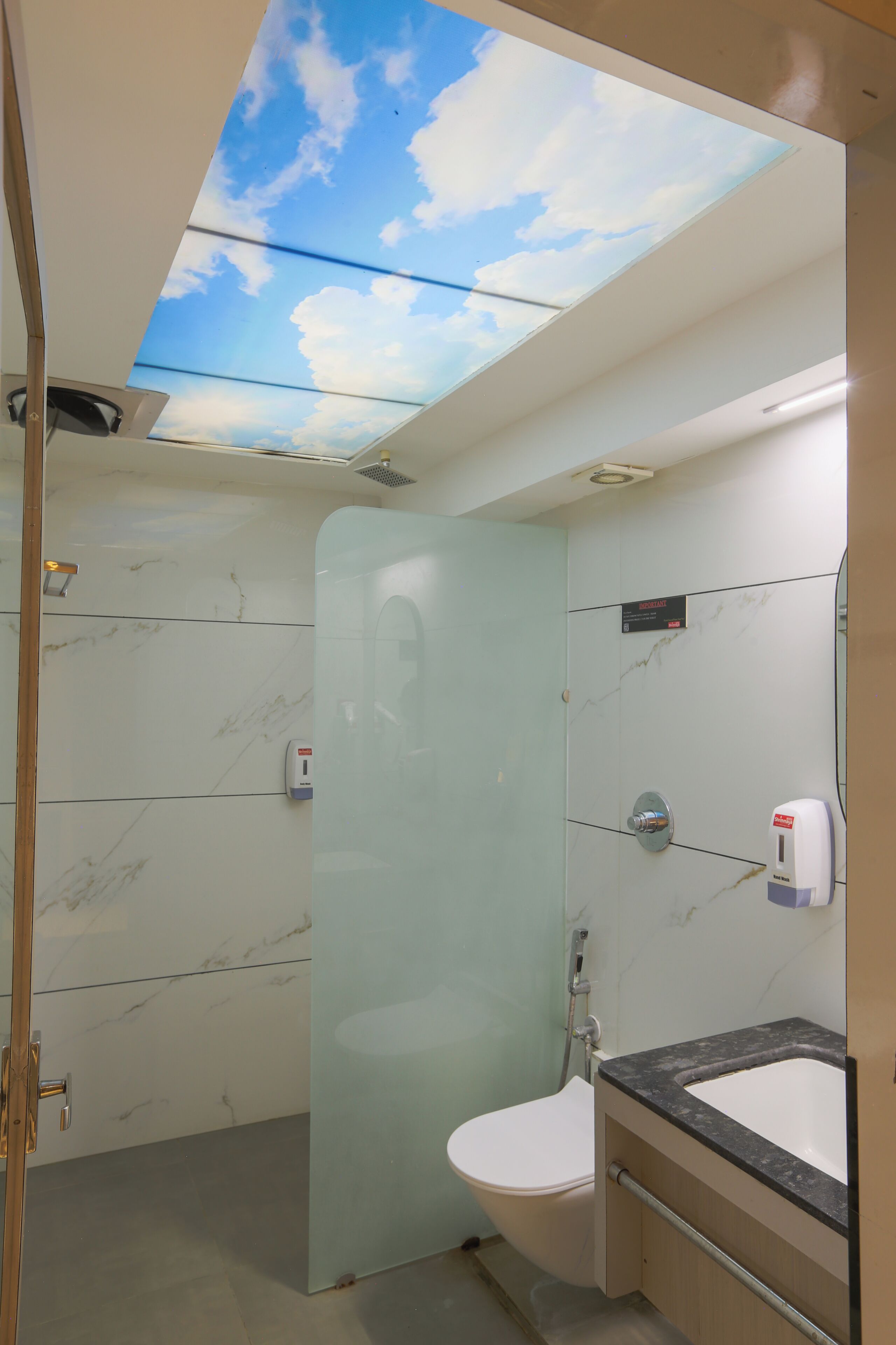 Un bagno con una cupola in vetro, box doccia in vetro, un water, un lavabo con piano in marmo e un dispenser di gel disinfettante.