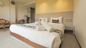 A hotel room with a large bed, a bedside table, a chair, a small table with a plant, and a clock on the wall. - Hotel Shrimmaya (Ujjain)