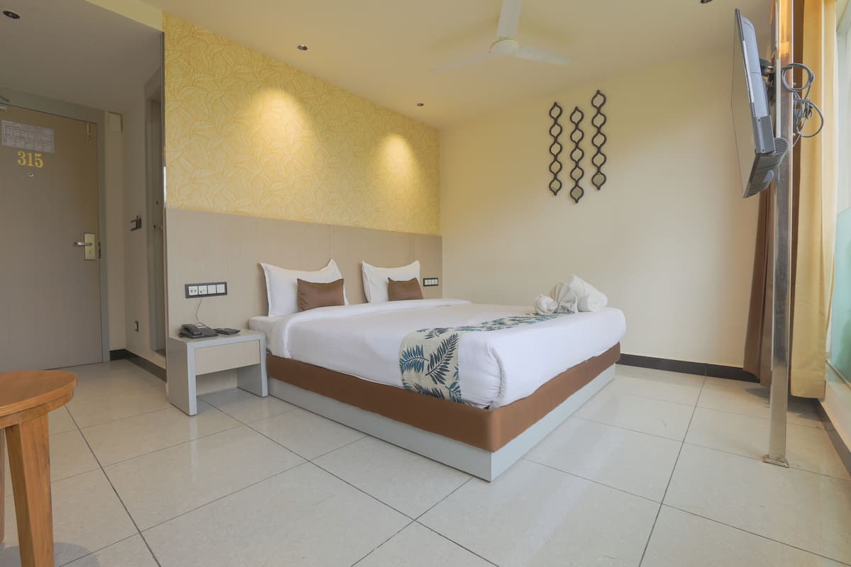 A hotel room with a bed, bedside tables, a desk, a chair, a TV, and a ceiling fan.
