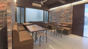 A restaurant with a stone wall, wooden furniture, and a ceiling fan. - Hotel Shrimmaya (Ujjain)