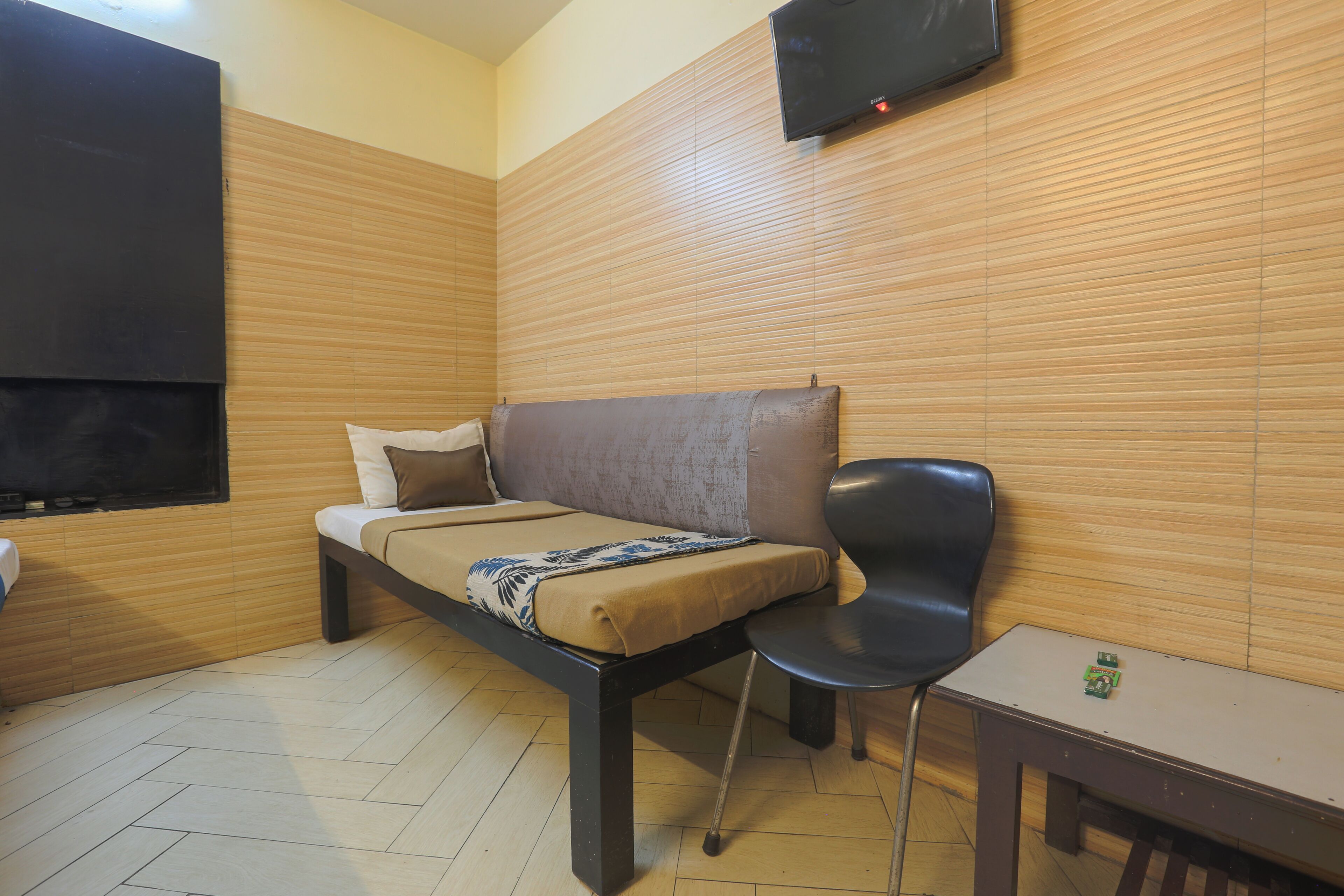 Una cama individual con cabecera, una mesita de noche, una silla y un televisor fijado a la pared.