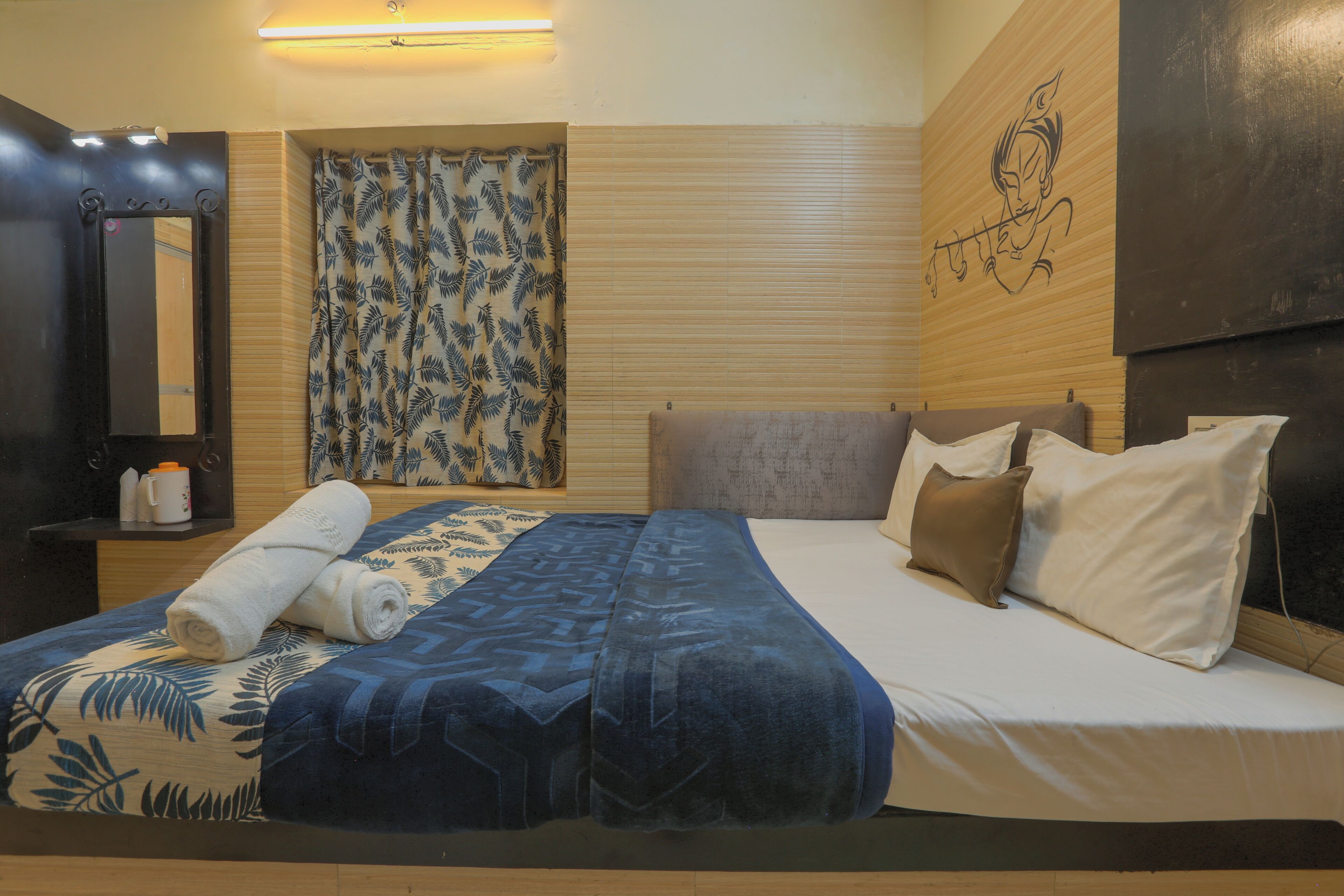 A bedroom with a bed, pillows, a towel, a window with blinds, a wall-mounted artwork, and a shelf with toiletries.