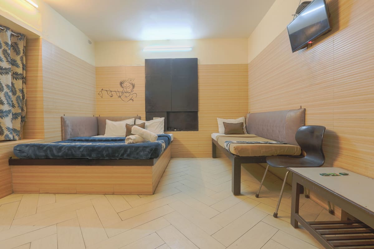 A compact room with a bed, a sofa, a chair, a small table, and a TV mounted on the wall.