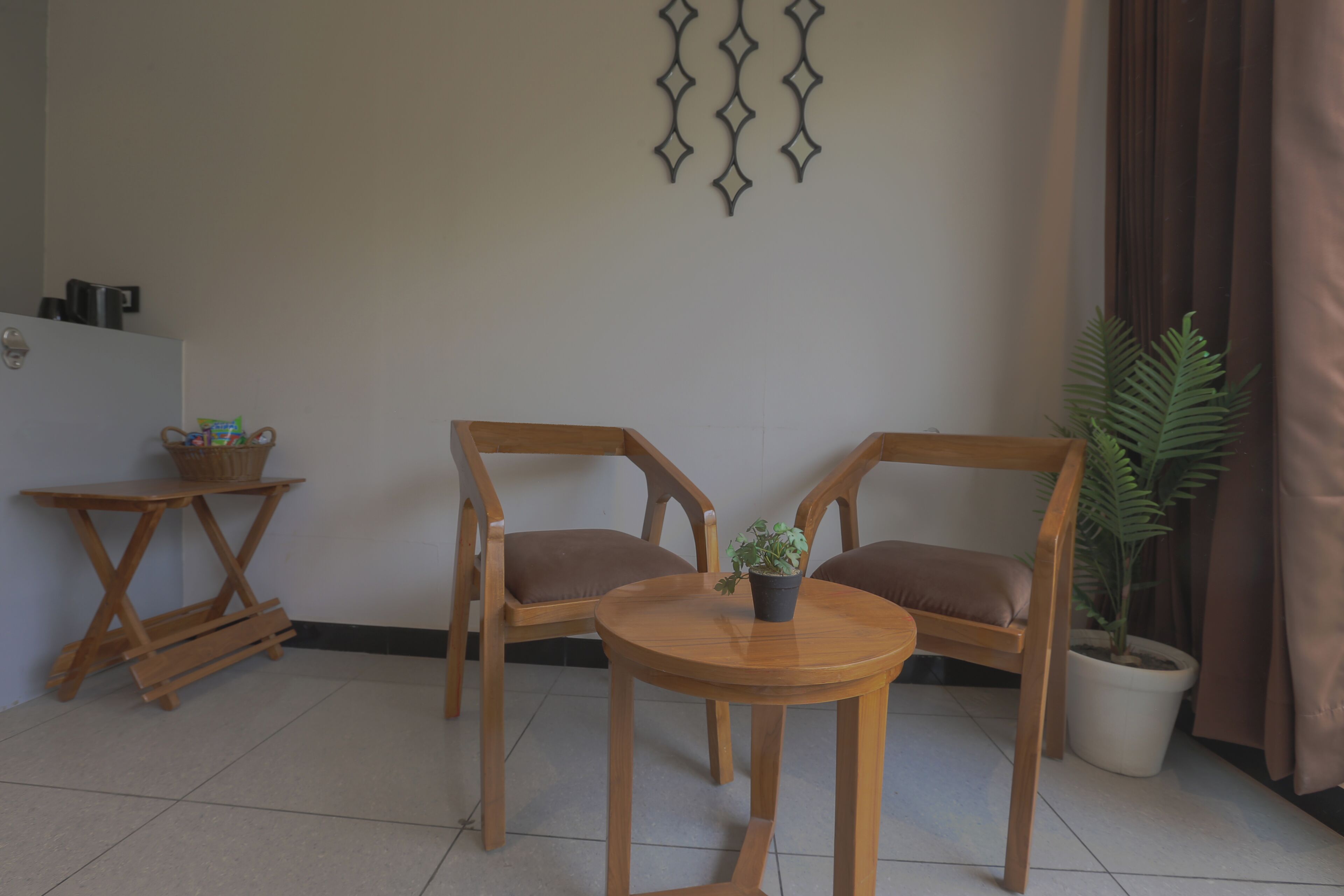 A room with two wooden chairs, a small round table with a potted plant, a wall-mounted decorative piece, and a potted plant by the window.