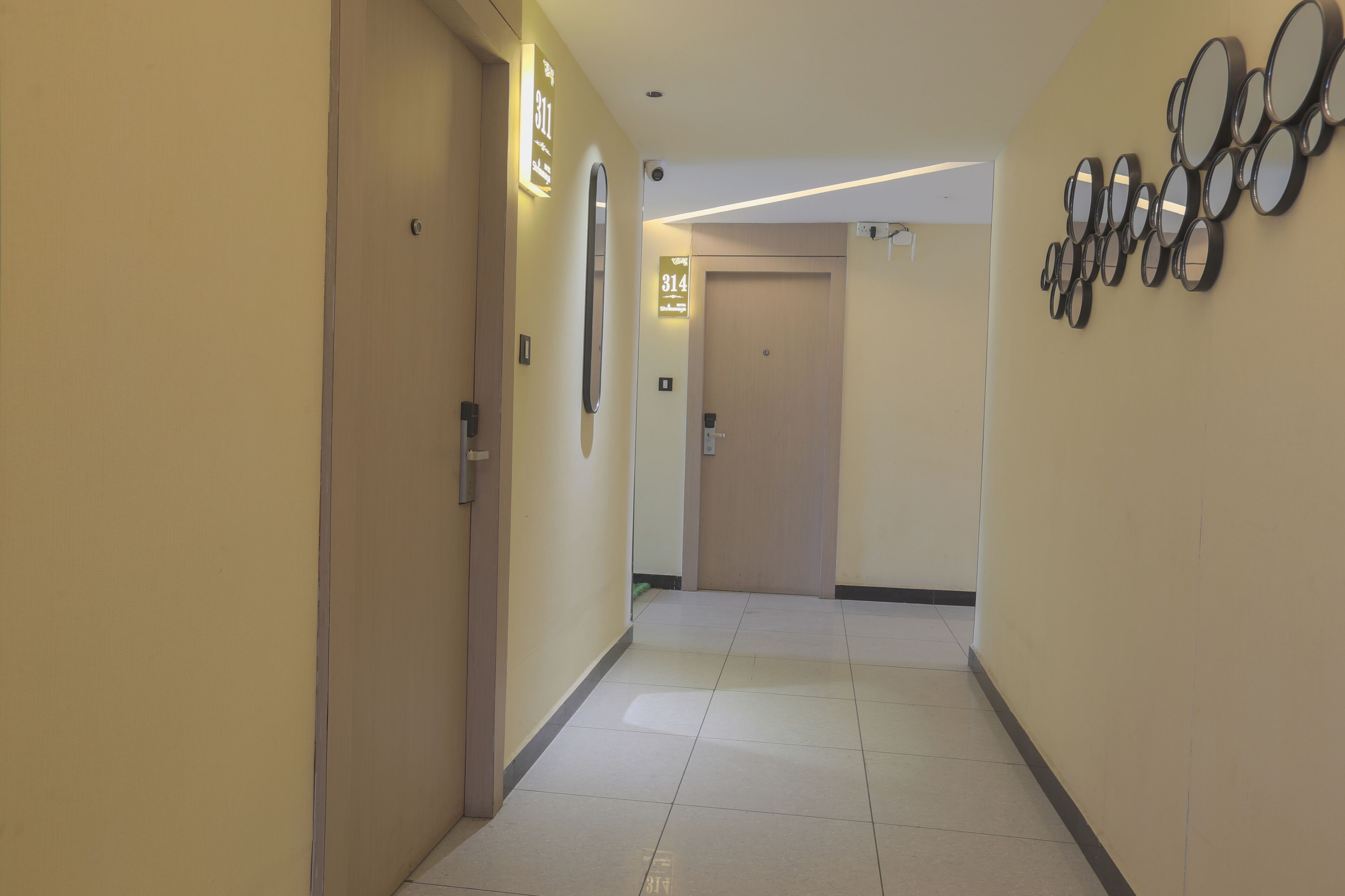 A hotel hallway with a door labeled '314,' a wall-mounted mirror, and a series of circular mirrors.