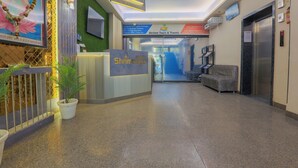 A hotel reception area with a reception desk, a seating area, and an elevator. - Hotel Shrimmaya (Ujjain)