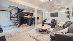 Un salon moderne avec un escalier en colimaçon, une cuisine en arrière-plan et un canapé gris avec une table basse.