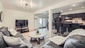 Un salon moderne avec un téléviseur, des canapés en cuir, une table basse et un escalier menant à la cuisine.