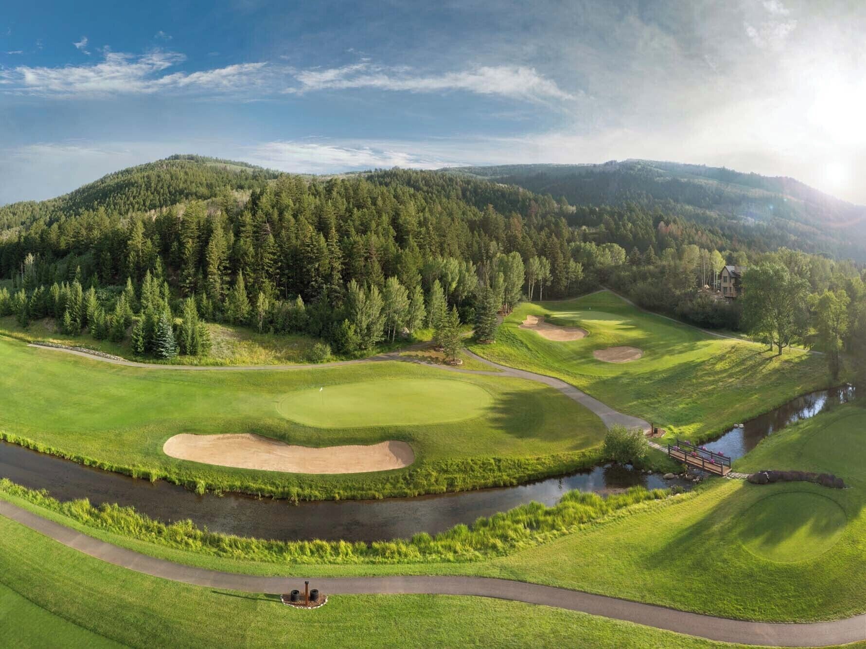Un campo de golf con múltiples áreas de juego, un cuerpo de agua y una colina boscosa al fondo.