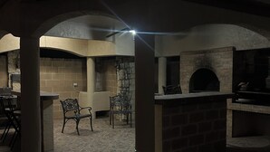 An outdoor patio area with a stone floor, a brick fireplace, and a ceiling fan. - Upstairs bar, palapa, 5 bedroom, king suite, Gig WiFi, great location  (Eagle Pass)