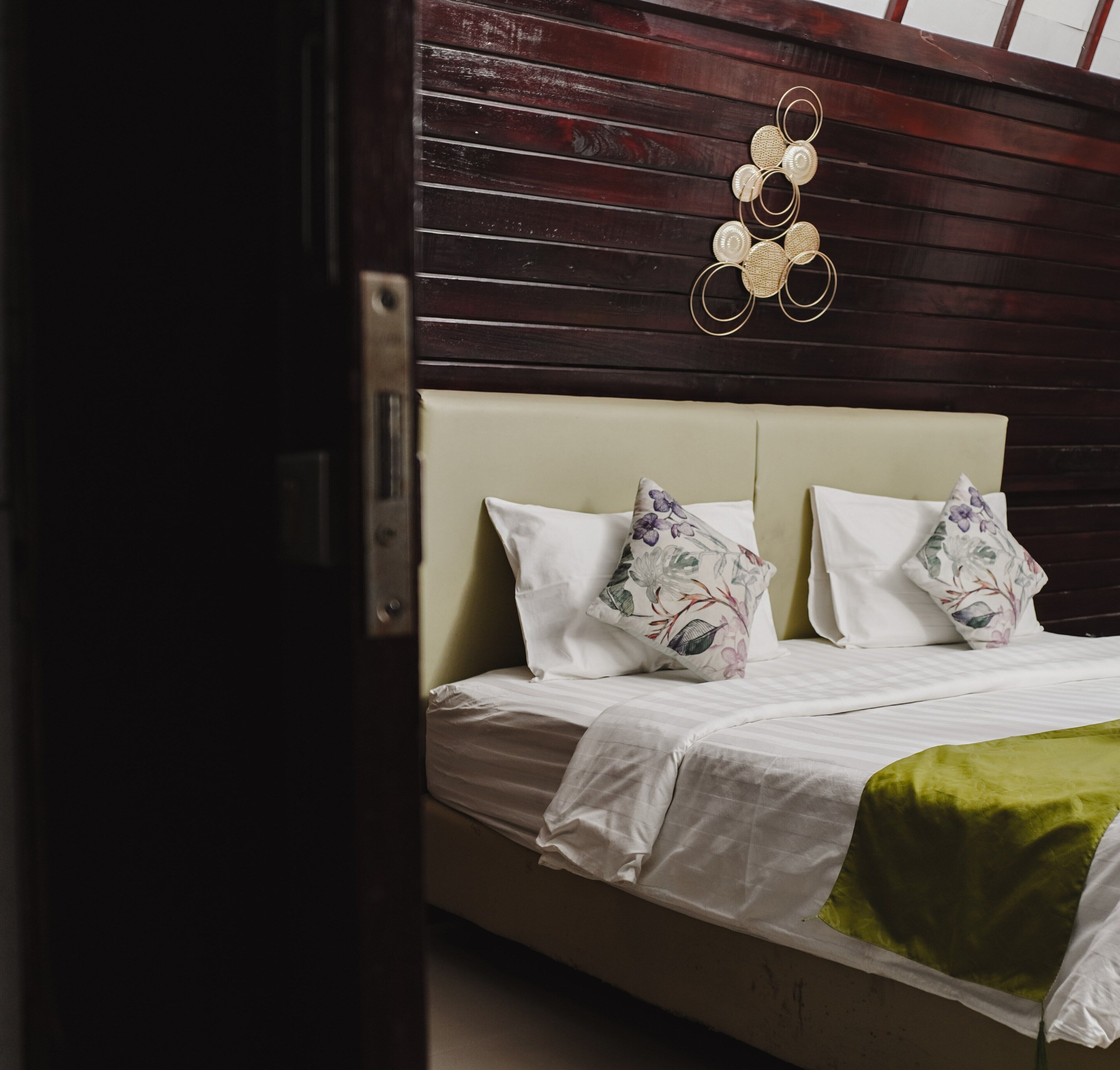 Uma cama com duas almofadas, um cobertor verde e um objeto decorativo fixado na parede.