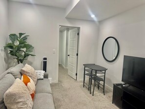 A living room with a sofa, a small table, a TV, and a door leading to another room.