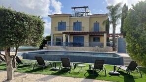 A two-story building with a swimming pool, outdoor seating, and a pergola.