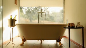 A bathroom with a freestanding bathtub, a small table with a glass and a bottle, and a statue on the wall.