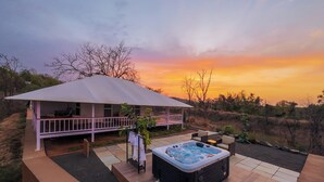 A hot tub and outdoor seating area with a covered porch, surrounded by a landscaped garden and a view of the sunset.