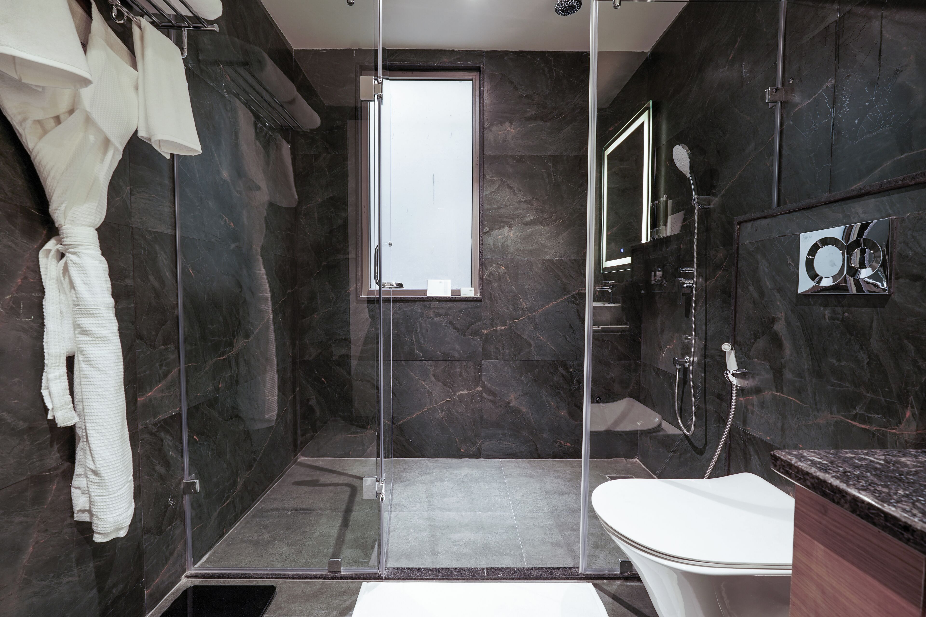 A modern bathroom with a glass-enclosed shower, a white toilet, and a marble wall.