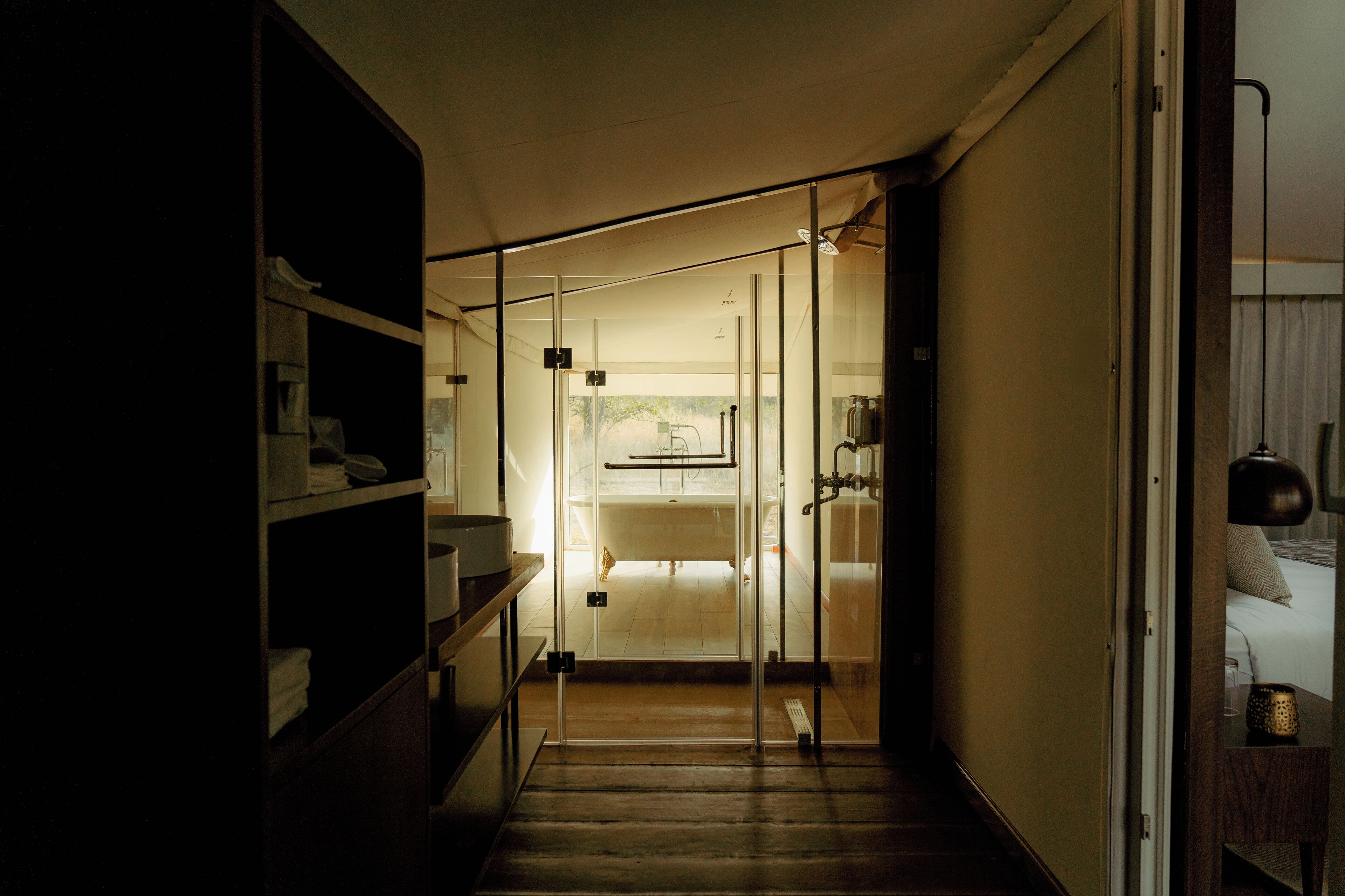 A narrow hallway leading to a room with a bed, a glass door, and a shelf with items.