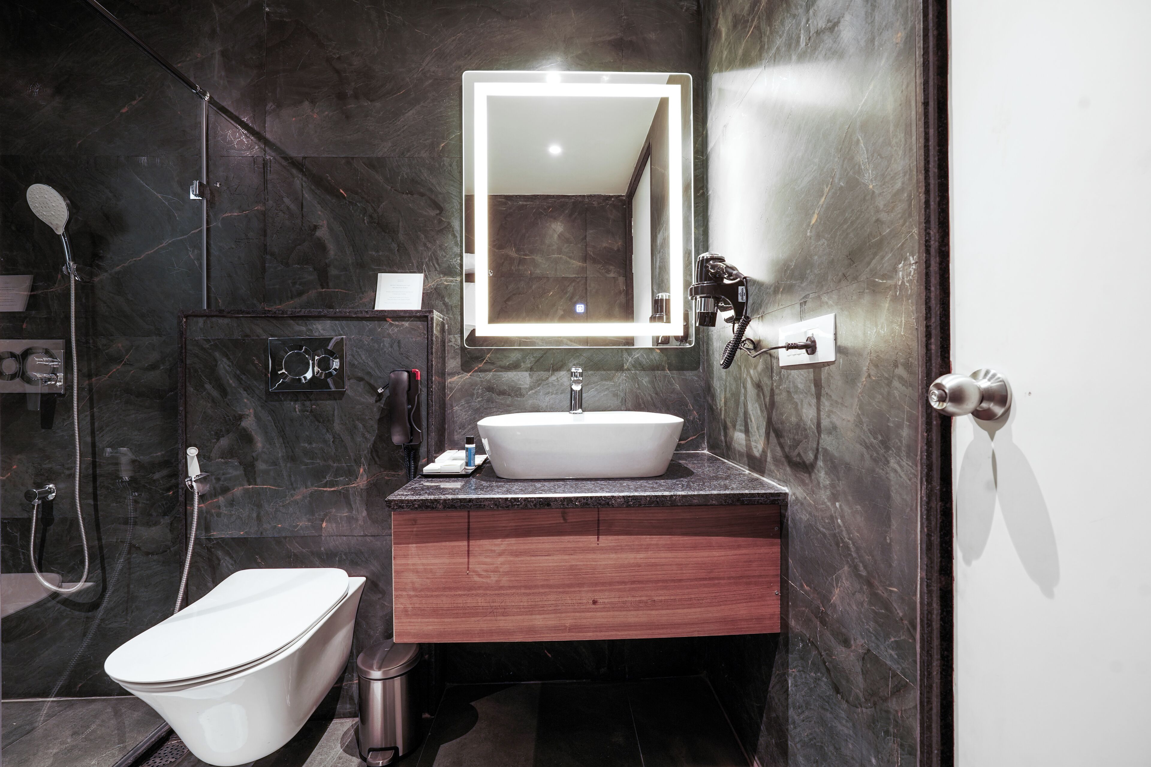 A modern bathroom with a freestanding toilet, a sink with a marble countertop, and a large mirror with integrated lighting.