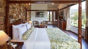 A spacious bedroom with a large bed, a wooden headboard, a stone wall, a dining area with chairs, and a view of the outdoors.