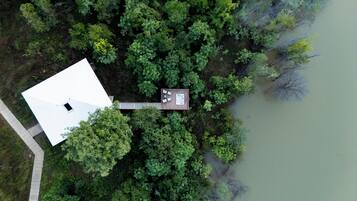 Vista aérea de una casa con terraza, rodeada por un bosque denso y una masa de agua.