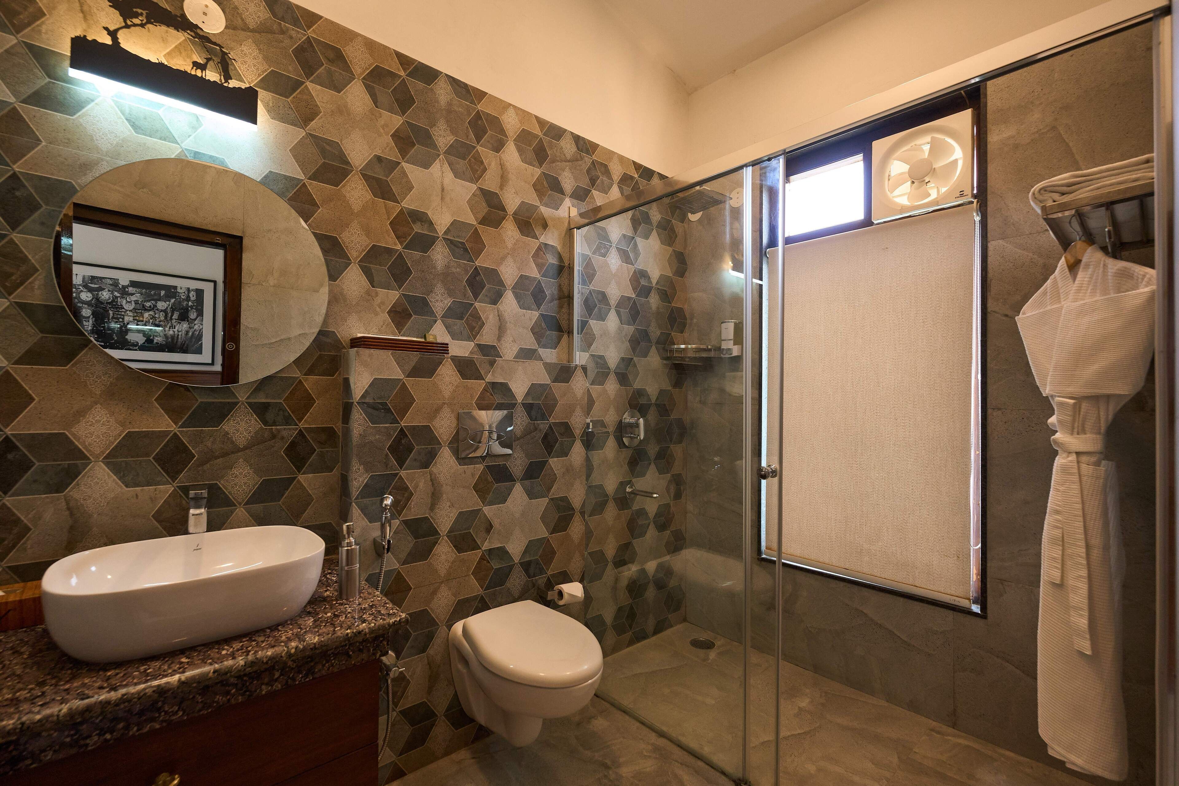 A modern bathroom with a geometric tile backsplash, a round mirror, a white sink, and a glass-enclosed shower.