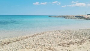 Una playa con agua turquesa transparente, orilla pedregosa y un promontorio rocoso al fondo.