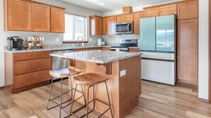 A modern kitchen with wooden cabinets, a granite countertop, stainless steel appliances, and a central island with stools. - Hendrix Hideaway on Rock Island Golf Course! (Rock Island)