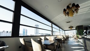 A modern restaurant with large windows, high ceilings, and a chandelier. Tables and chairs are arranged for dining. - Alion Hotel (Izmir)