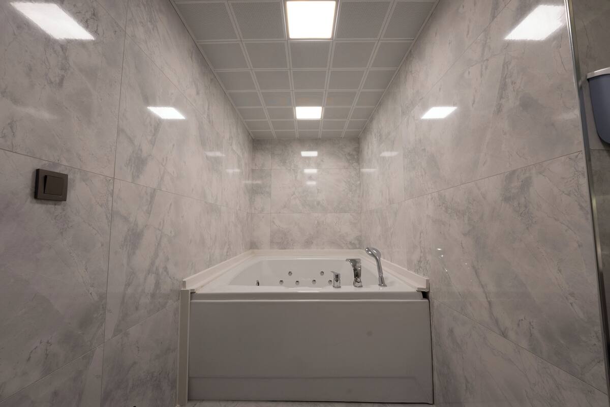 Ein modernes Badezimmer mit einer großen Badewanne, Marmorwänden und einer Decke mit Einbaustrahlern.