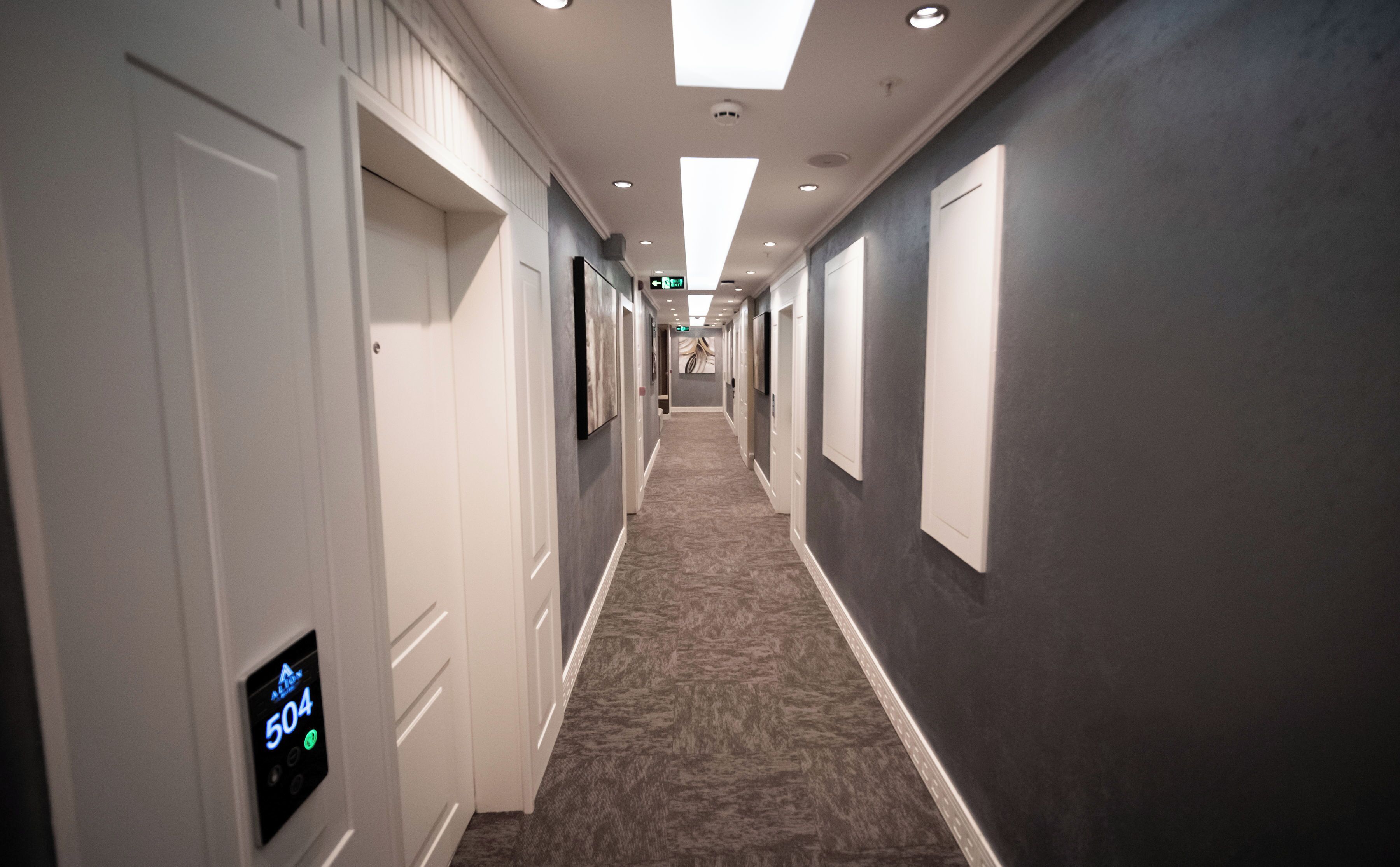 A hotel hallway with a carpeted floor, white doors, and a digital display showing the number 504.