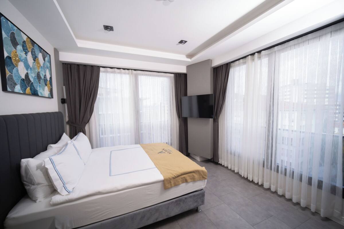 Ein modernes Hotelzimmer mit einem Bett, Vorhängen, einem Fernseher und einem Gemälde an der Wand.