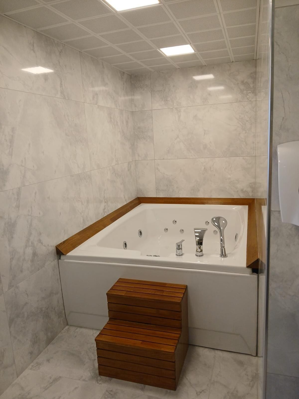 A modern bathroom with a freestanding bathtub, wooden steps, and a glass shower enclosure.