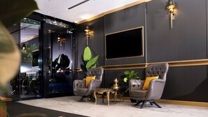 A modern lobby with leather armchairs, a gold table, and a large TV on the wall. - Alion Hotel (Izmir)